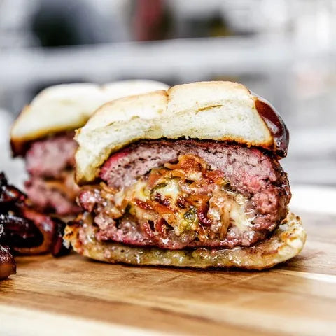 Close-up of a juicy burger with melted cheese and bacon on a wooden cutting board.